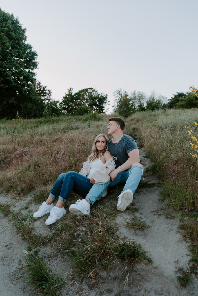 A couple sitting in a field with the woman leaning up against the man as he is looking off into the distance during their Seattle engagement photos