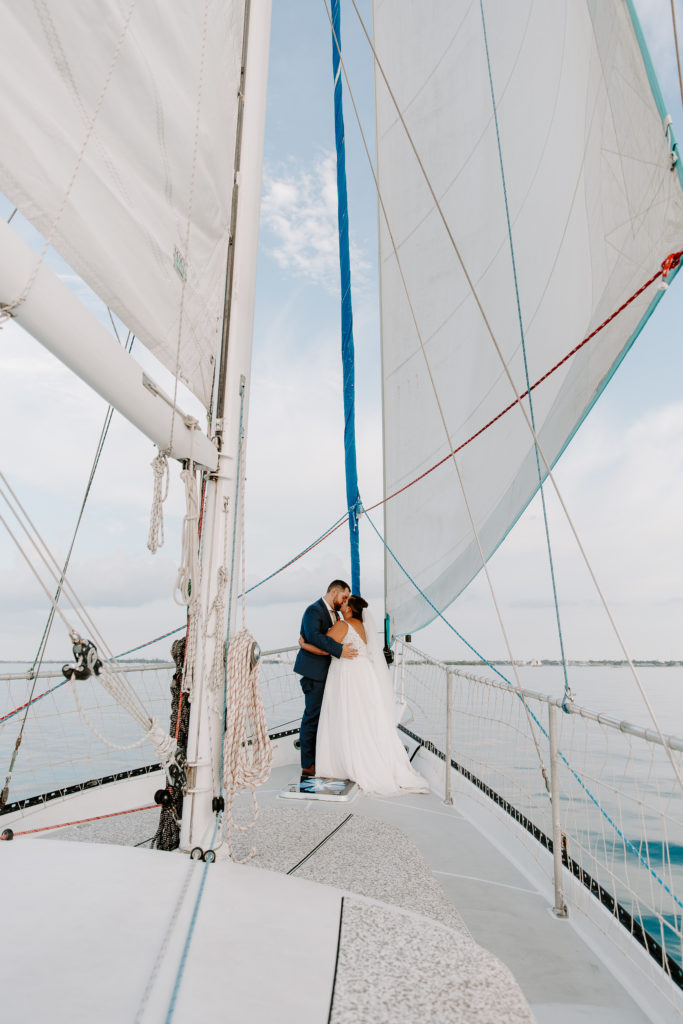 A couple in wedding attire sharing a kiss at the front of a sail boat during their all day florida keys elopement