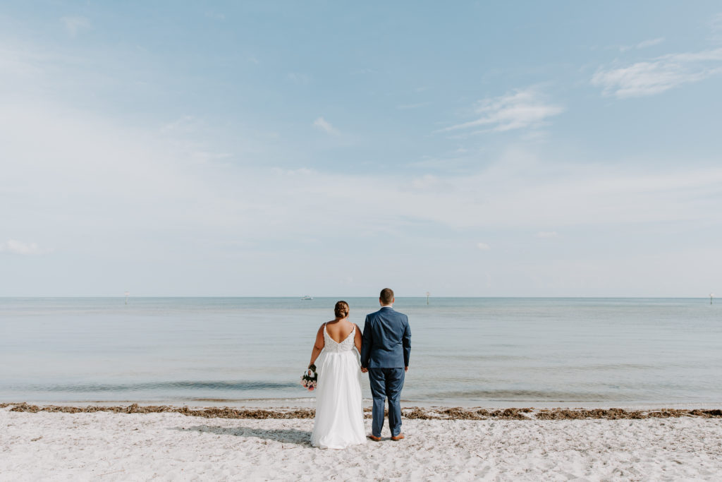 A couple in wedding attire holding hands and looking out at the beach during their key west elopement