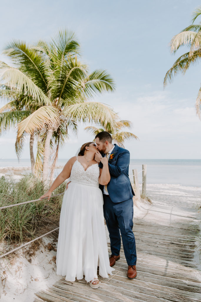 A man bringing his partner in for a kiss with the ocean and palm trees in the background during their Smathers beach elopement