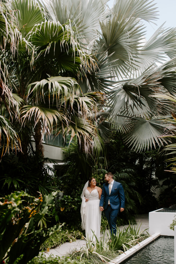A couple holding hands and smiling at each other surrounded by palm trees during their first look of their florida elopement
