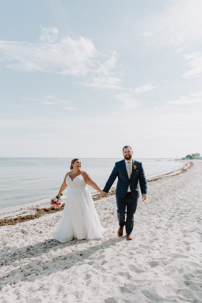 A man and a woman holding hands laughing as they walk along Smathers beach during their key west elopement