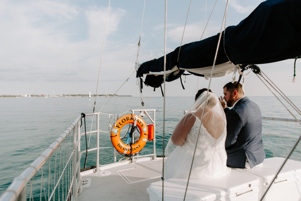 A newly wed couple sitting on the back of a sail boat drinking champagne during their all day key west elopement