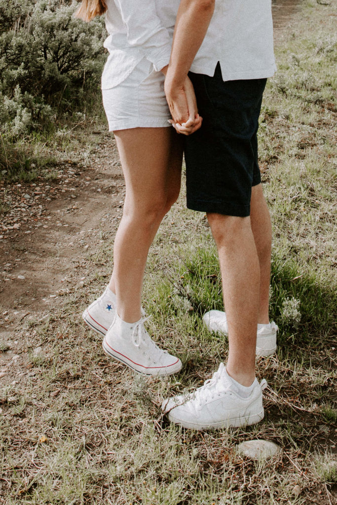 A couple wearing matching white converse and holding hands during their Wyoming engagement photos
