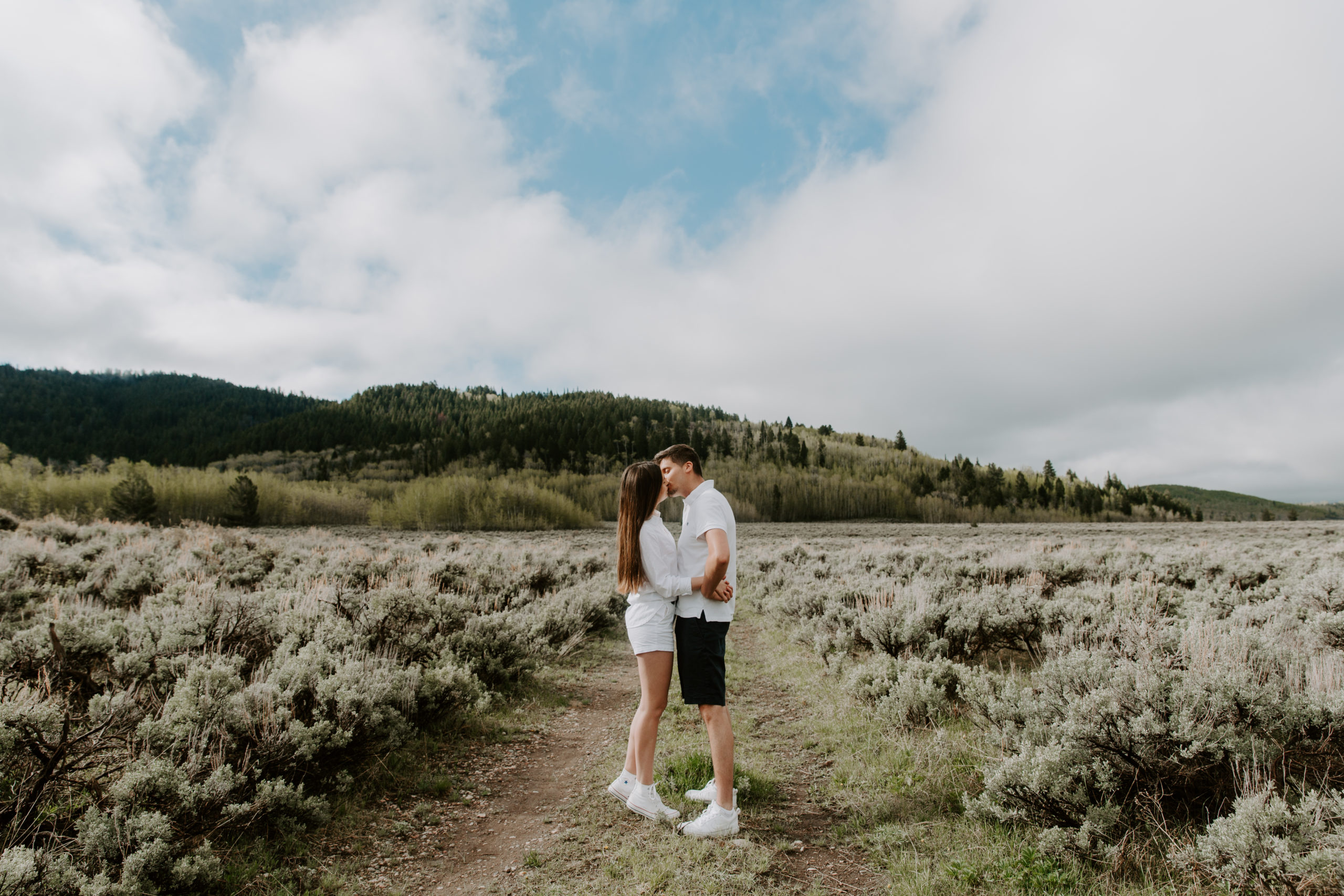 A couple standing in a field facing each other as they share a kiss with the mountains behind them in Wyoming