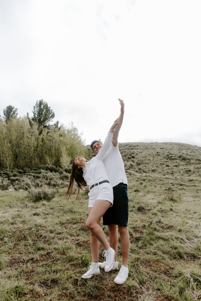 A couple standing on a hill with their arms out stretched and intertwined as they act like an airplane during their sunrise couple photos in Jackson Hole, Wyoming