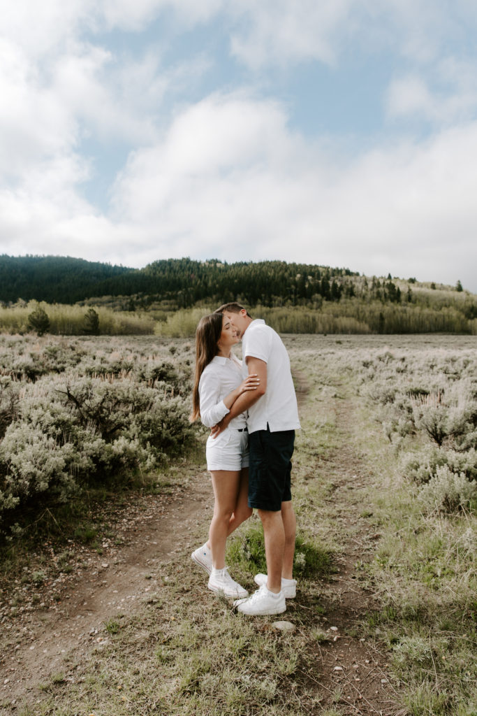 A man whispering into his partners ear while he has his arms around her during their Grand Teton National Park engagement photos