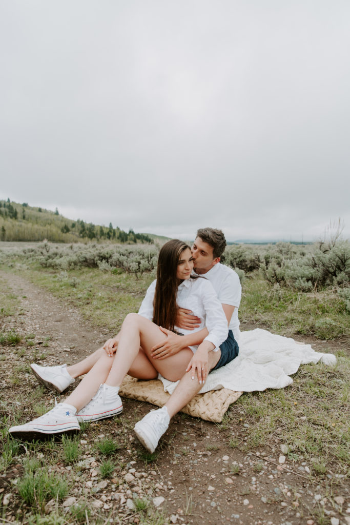A couple sitting on a blanket with the woman in the mans lap during their Wyoming engagement photos