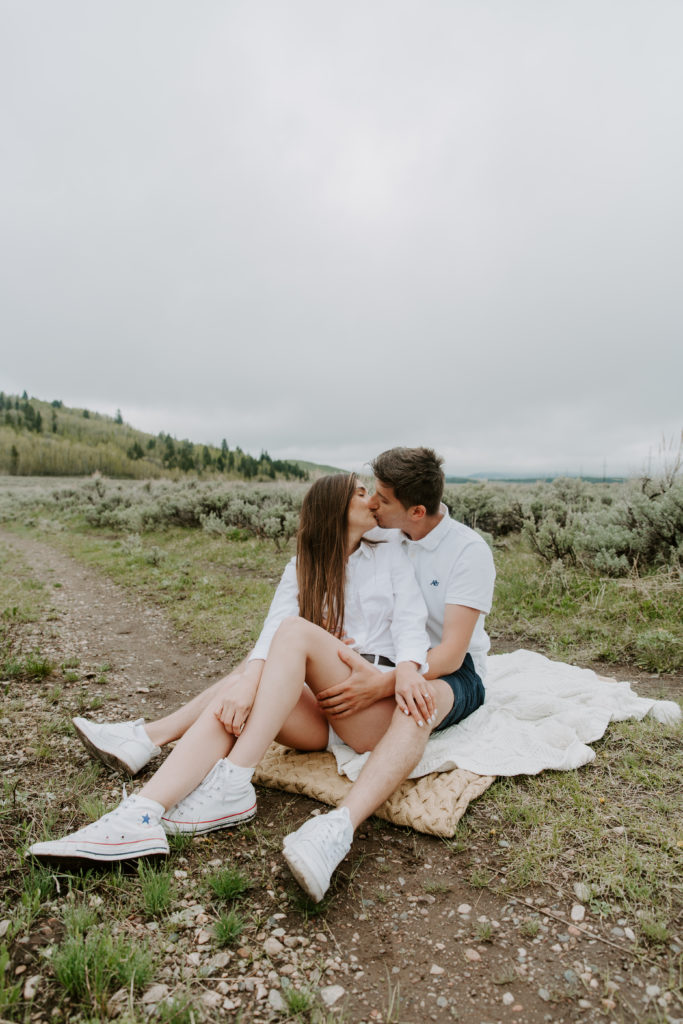 Couple sitting on a blanket in a field sharing a kiss during their Jackson Hole couple photos in Wyoming