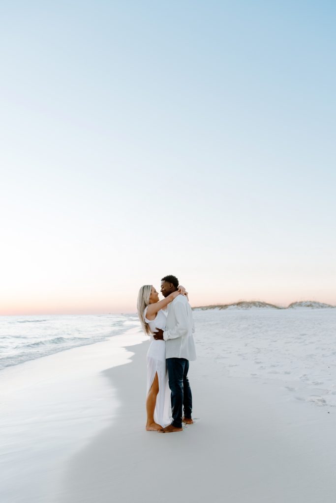 Couple standing face to face with the woman arms wrapped around her partner as they are looking at each other during their beach couple photos