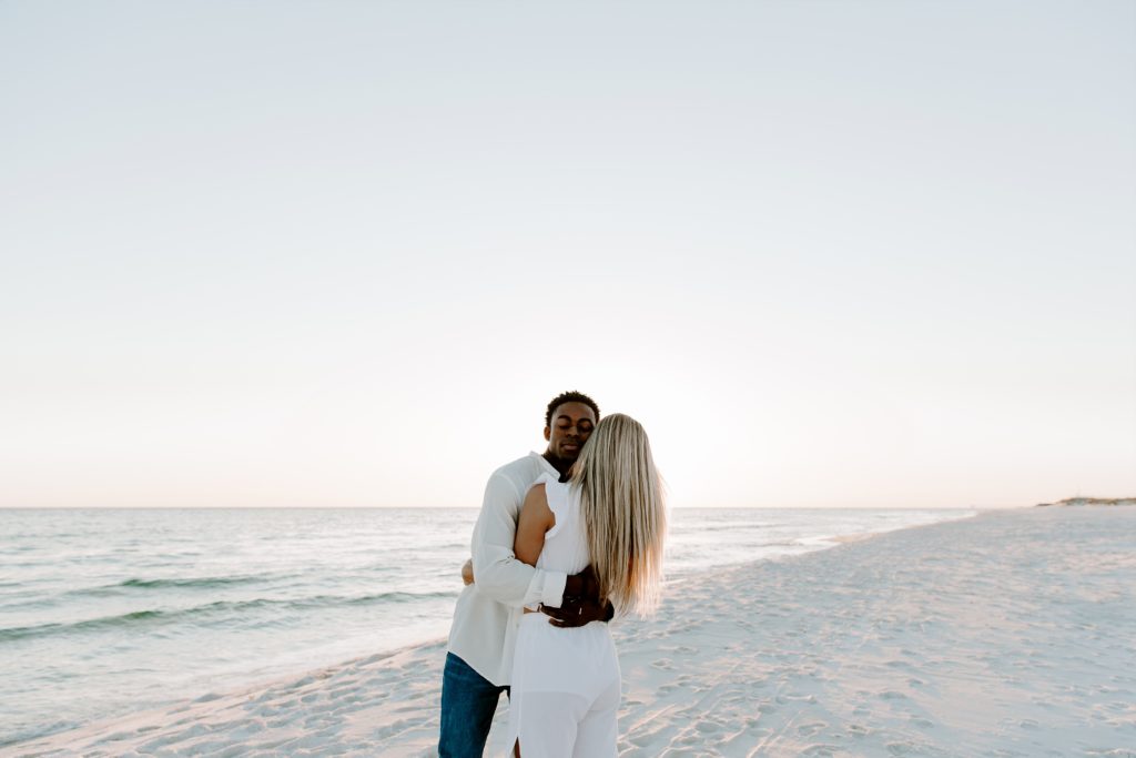 Man hugging on his partner tightly with his eyes closed as the sun flares around them during their beach couple photos during their winter photos in Florida