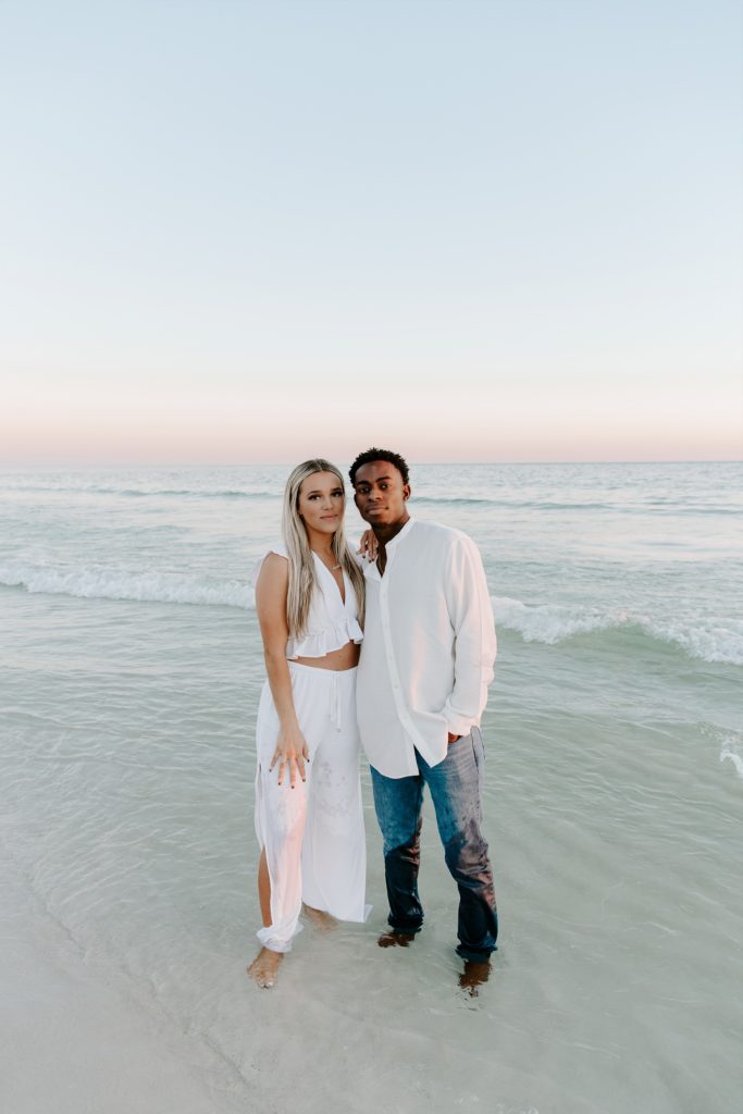 A man and a woman standing in the ocean with their arms around each other soft smiling during their Florida panhandle couple photos