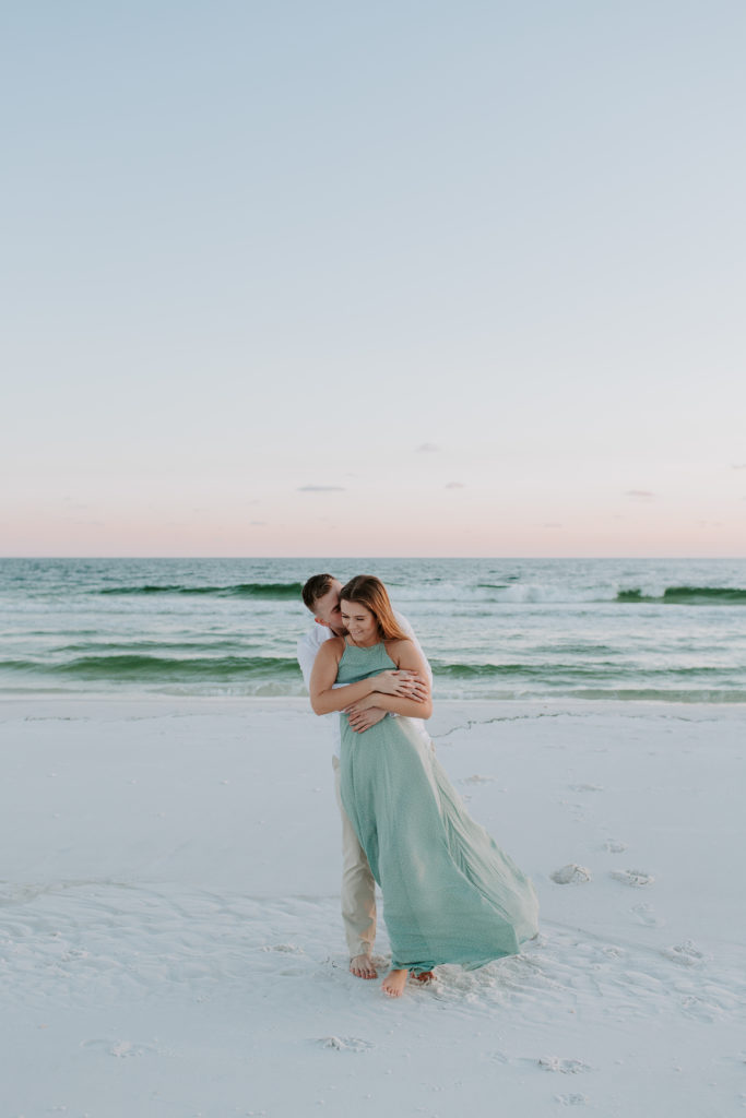 Man hugging his partner from the back as she is laughing during their beach engagement photos in the Florida Panhandle