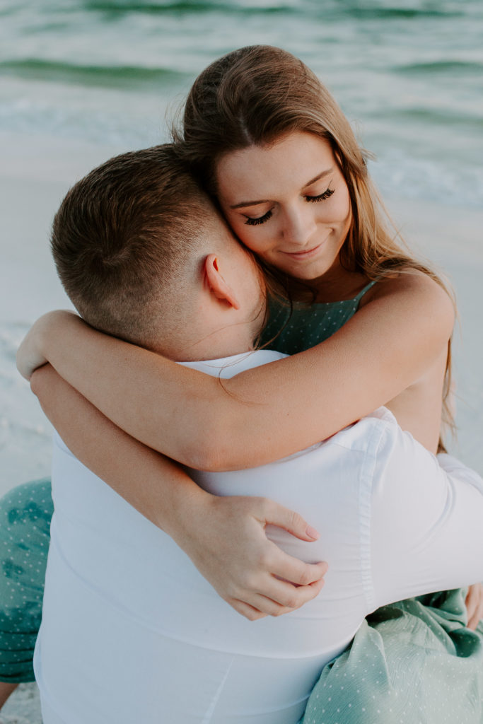 Woman hugging onto her partner with their eyes closed during their beach engagement photos in Destin, Florida