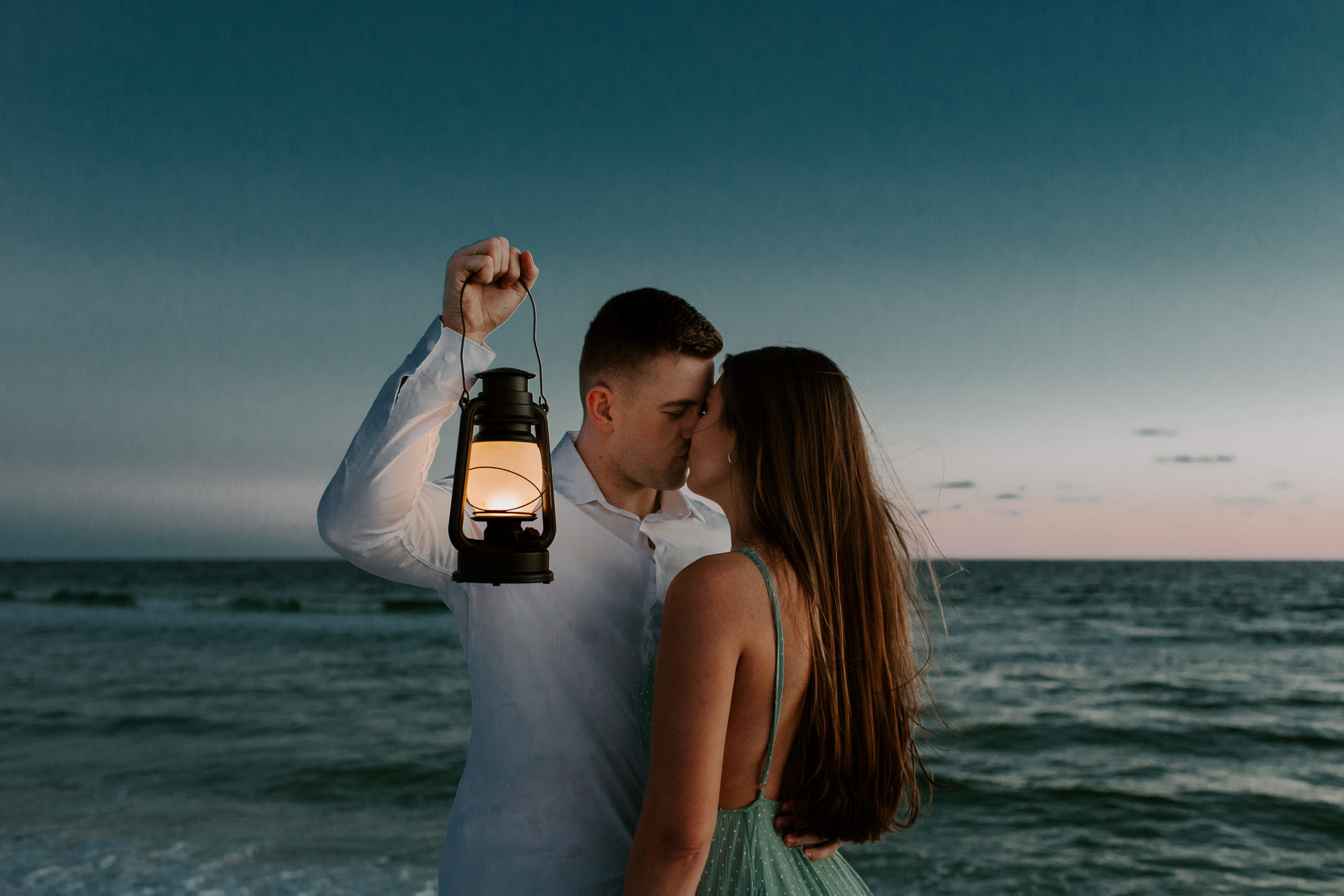 Man giving his partner a kiss while holding up a lantern during their Destin beach engagement photos