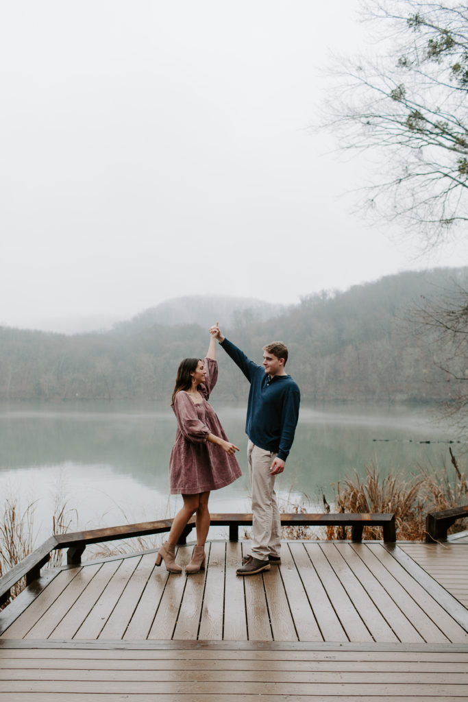 Man spinning his fiancé in a circle on a dock with the mountains rolling in the background during their winter engagement photos