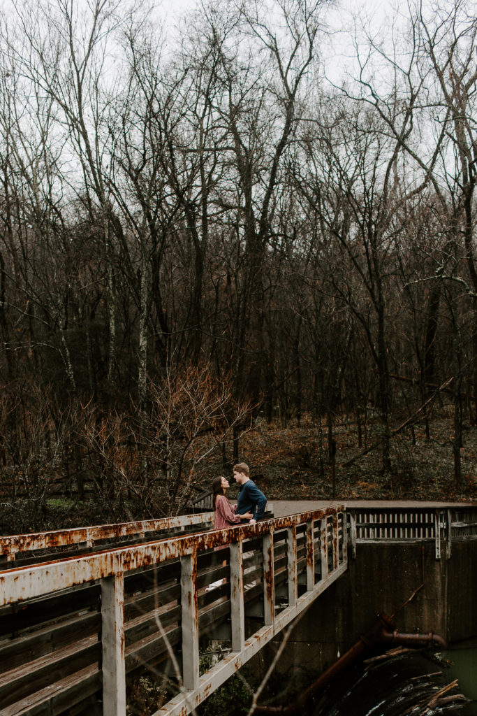 Couple standing on a bridge over a waterfall as they are leaning into each other during their Nashville, Tennessee engagement photos