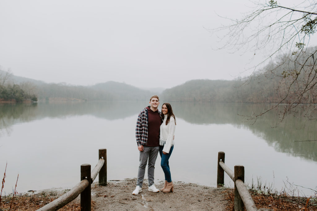 Couple standing at the edge of a lake with their arms around each other and they are both smiling during their state park couple photos in Tennessee