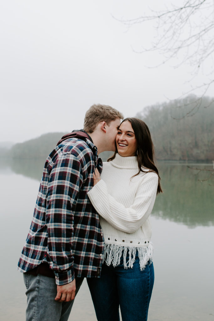 Man whispering into his partners ear as she has her hand on his chest and laughing during their Tennessee engagement photos