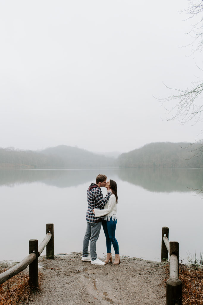 Man and woman sharing a kiss at the edge of a lake with the reflection in the water during a Radnor State Park couple session