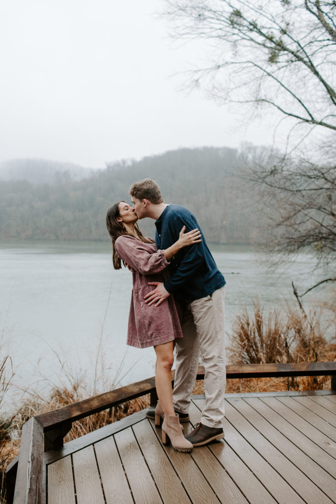 Man dipping his partner at the waters edge and bringing her in for a kiss with the hills in the background during their Radnor Lake State Park engagement photos