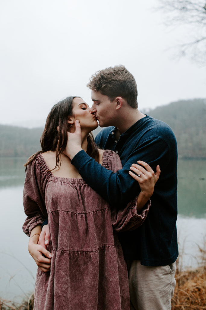 Man bringing his fiancé in for a kiss as he holds her hip during their winter engagement photos