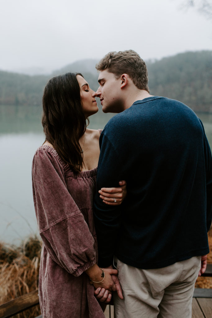 Couple going in for a kiss as they are holding hands with the hills in the background during their Nashville engagement photos