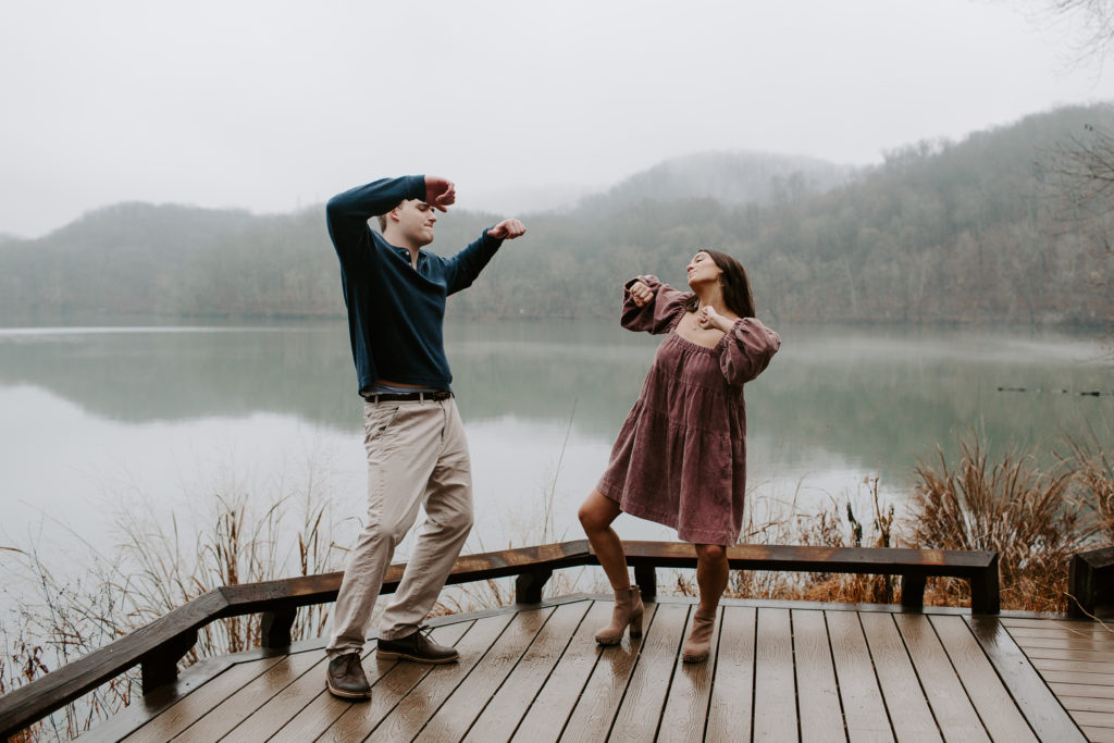 Couple dancing goofy on a dock at the waters edge during their winter engagement photos in Tennessee