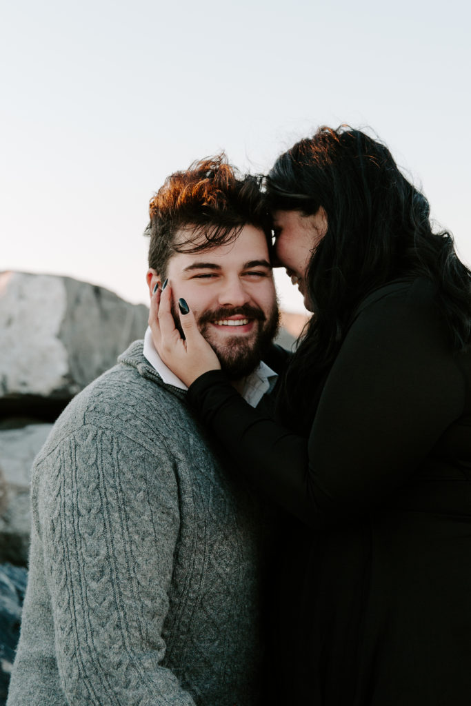 Woman nuzzling into her partners face as she is holding his cheek and he is laughing during their beach engagement photos in Destin