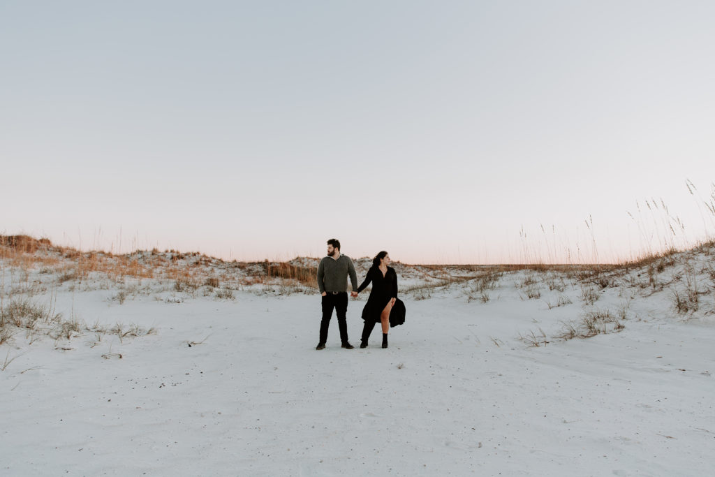 Couple standing in a wide space with sand dunes on each side during their winter couple photos in Florida