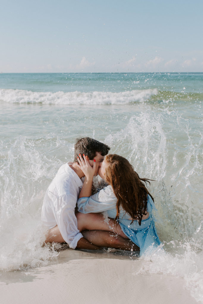 Couple sitting near the water and sharing a kiss as the waves crash around them during their Destin proposal