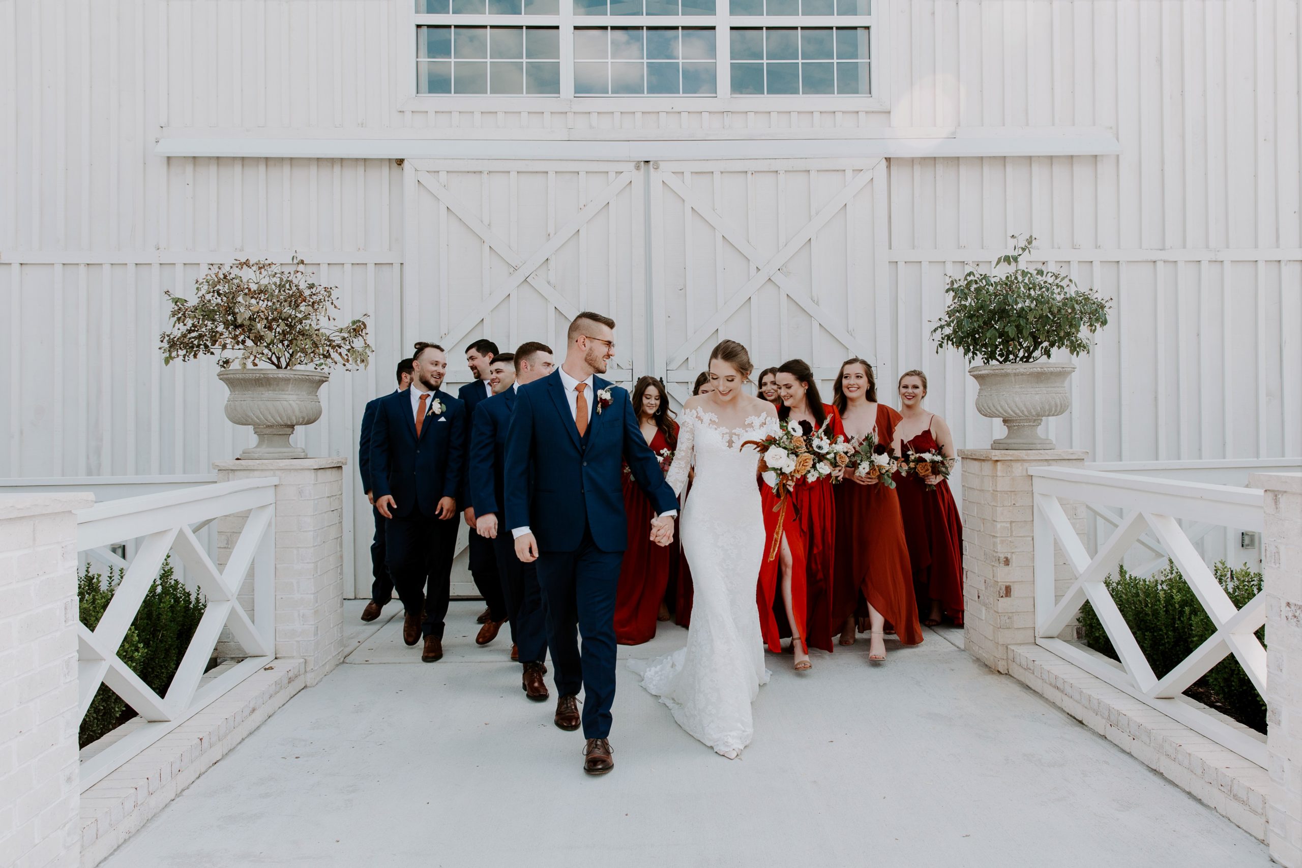 Couple holding hands and walking along a path with their wedding party