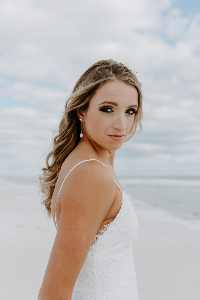 Bride holding her hands behind her back as she is looking over her shoulder during her beach portraits along the emerald coast in Florida