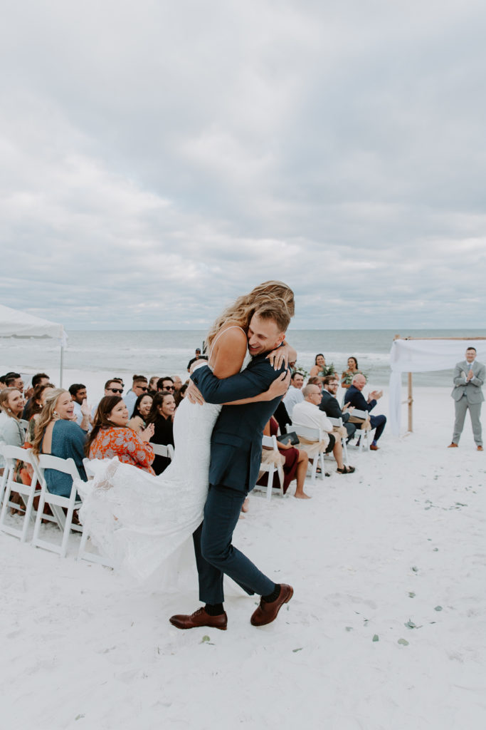 Groom holding his bride and carrying her down the aisle after they finished their vow renewal on the beach in Florida