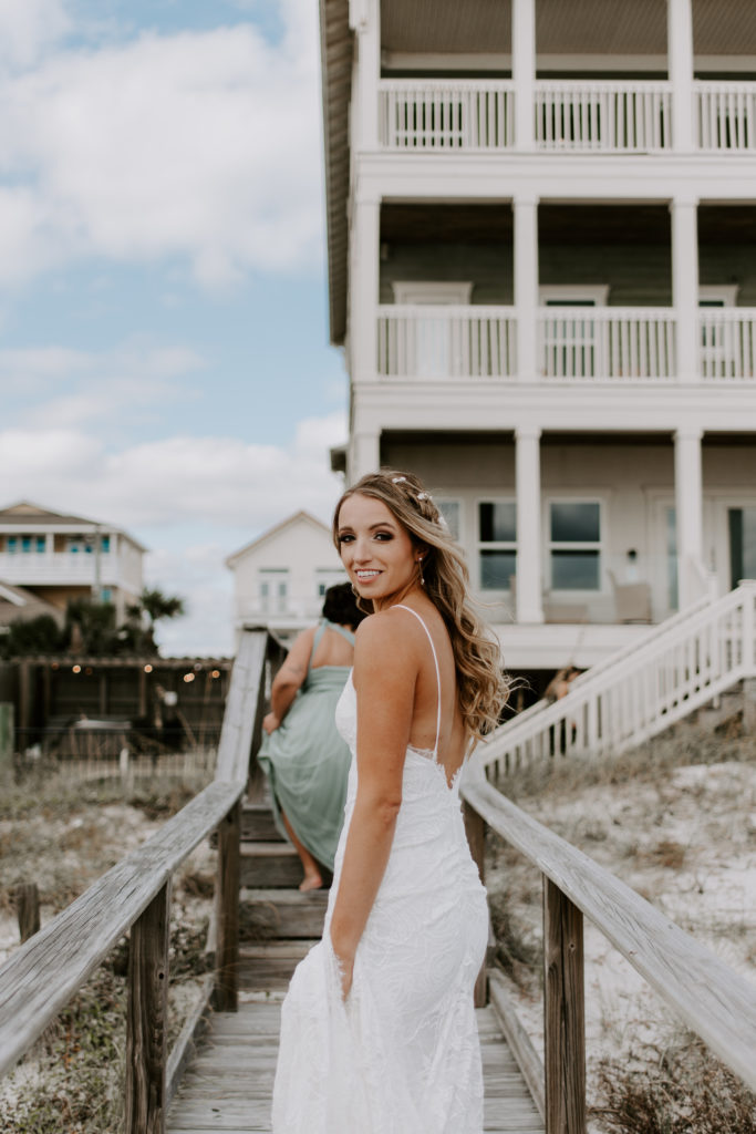 Bride looking back over her shoulder as she and her bridesmaids are walking along the boardwalk to the beach rental house during her Florida wedding