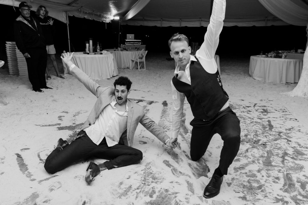 Groom and best man sliding cross the dance floor that is covered in sad