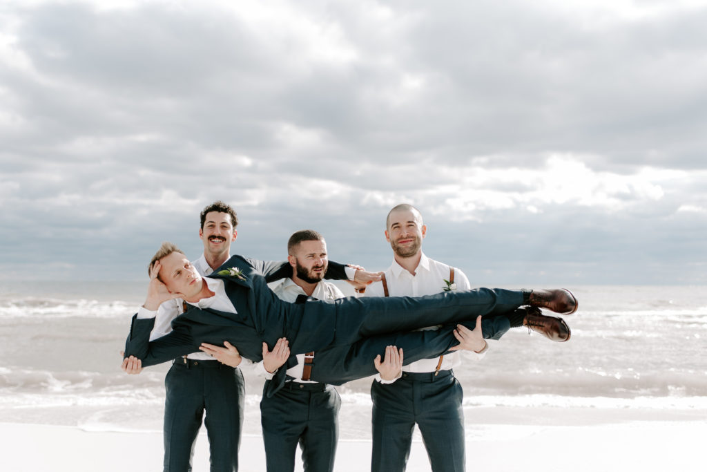 Groomsman holding up the groom as they are standing on the beach in Destin, Florida