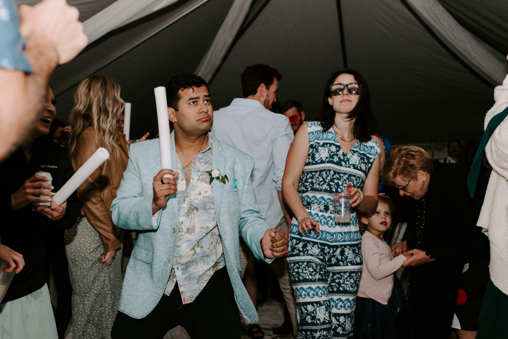 1 guest with sunglasses on and 1 guest waving around a glow stick during a beach front wedding reception