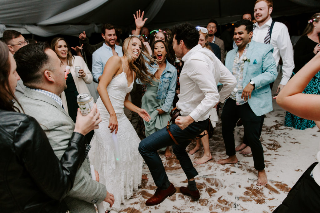 Bride and best man having a dance off as they are surrounded by their friends during their beach wedding