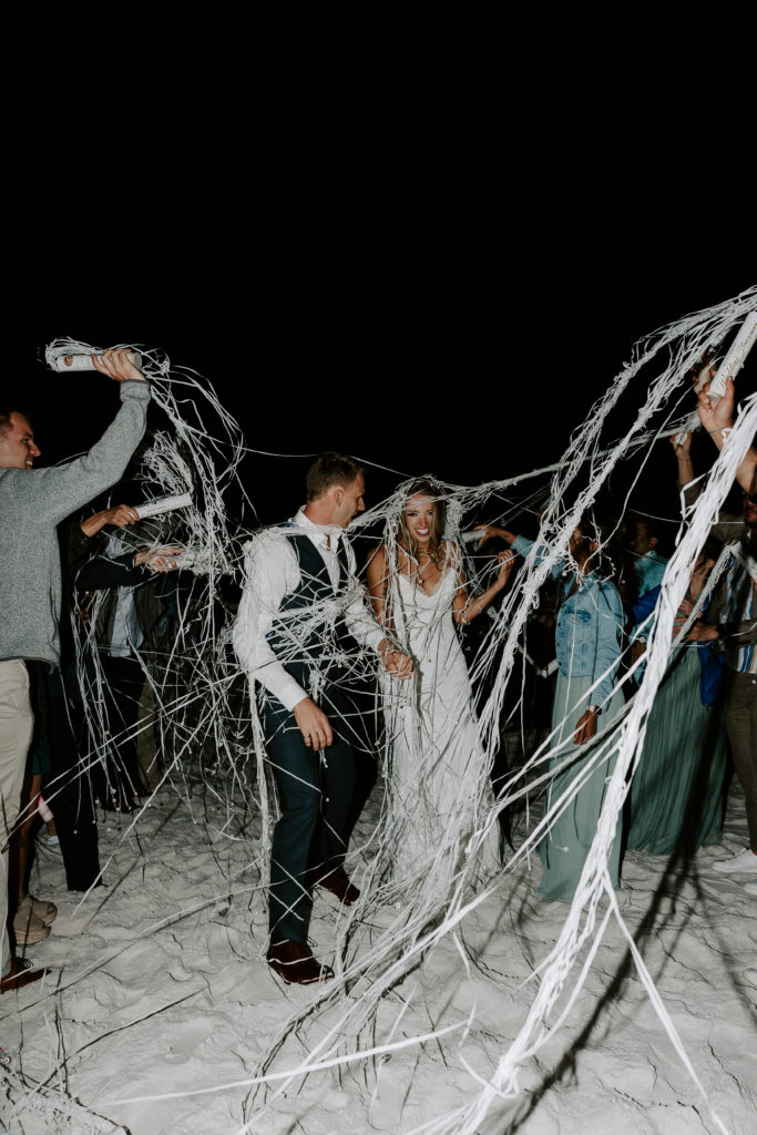 Couple running through their guests who have made a tunnel for them to go through as they are throwing streamers at them