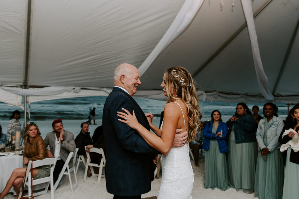 Father of the bride smiling as he is dancing with her during the beach front reception
