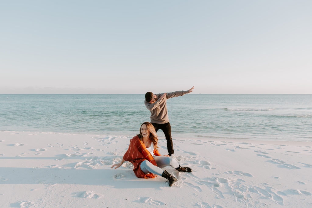 Man dabbing as his partner is spinning in circles on the ground as they are dancing during their beach couple photos in Florida