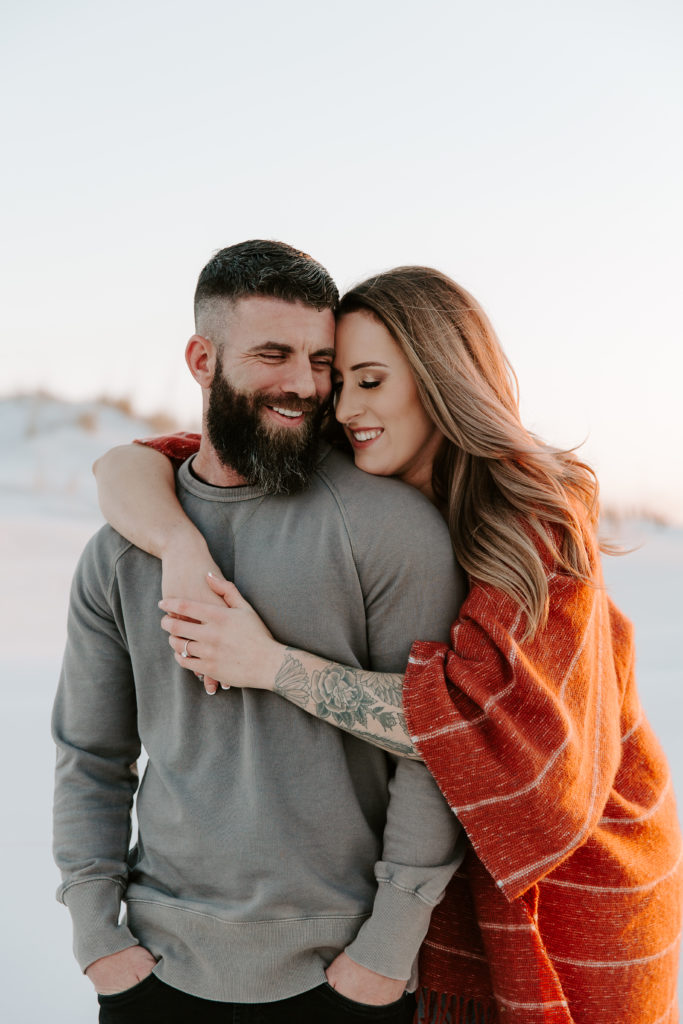 Woman holding onto her partner with her arms wrapped around him with their foreheads leaning against each other as they are laughing during their Destin engagement photos