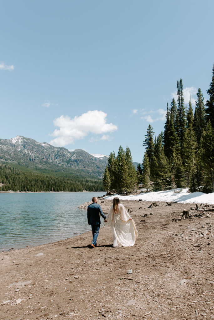 Couple holding hands and walking along the lake side during their Montana elopement