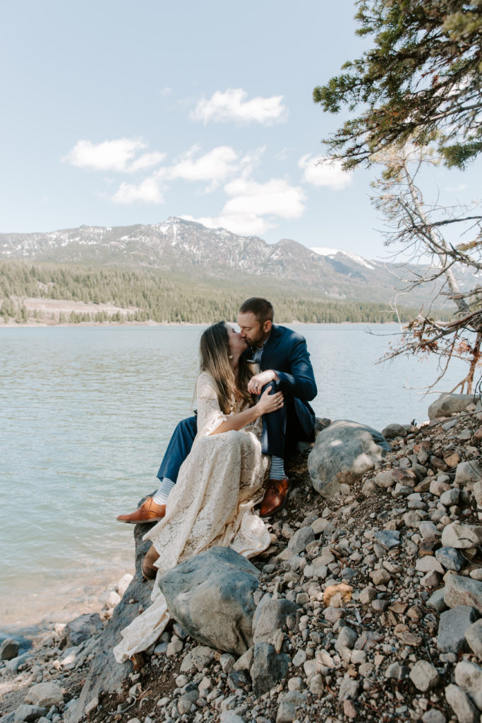 Couple sitting on the edge of a rocky embankment as they share a kiss during their mountain elopement