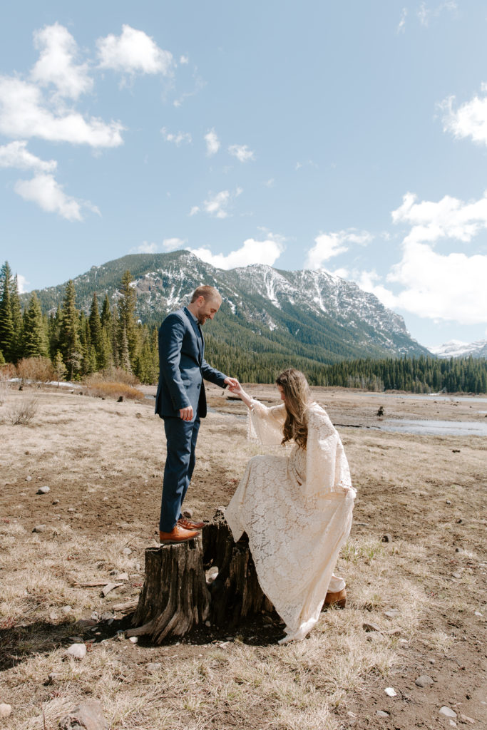 Man helping his partner get up onto the stump he is standing on during their Montana elopement
