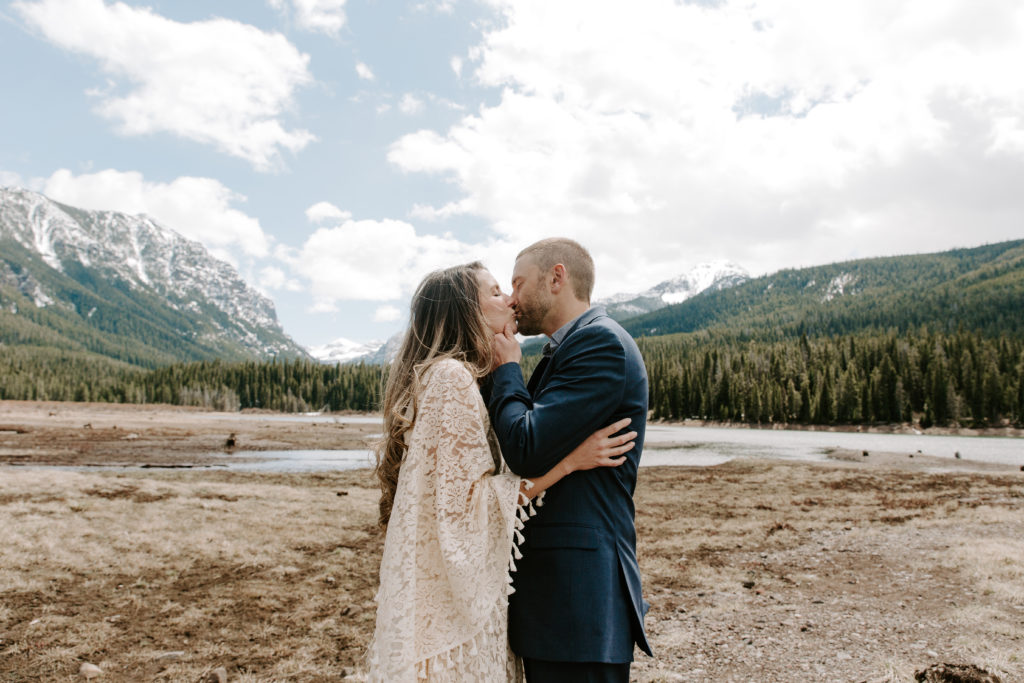Couple sharing a kiss as the man holds onto his partners face with the mountains in the background during their lake elopement