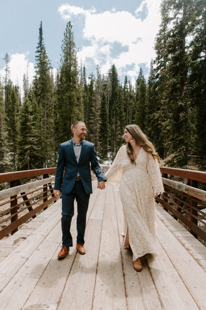 Man and woman holding hands and walking along a bridge smiling at each other during their adventure elopement
