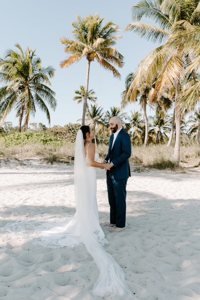 Couple standing facing each other and holding hands as they are doing their first look on the beach in the Florida Keys