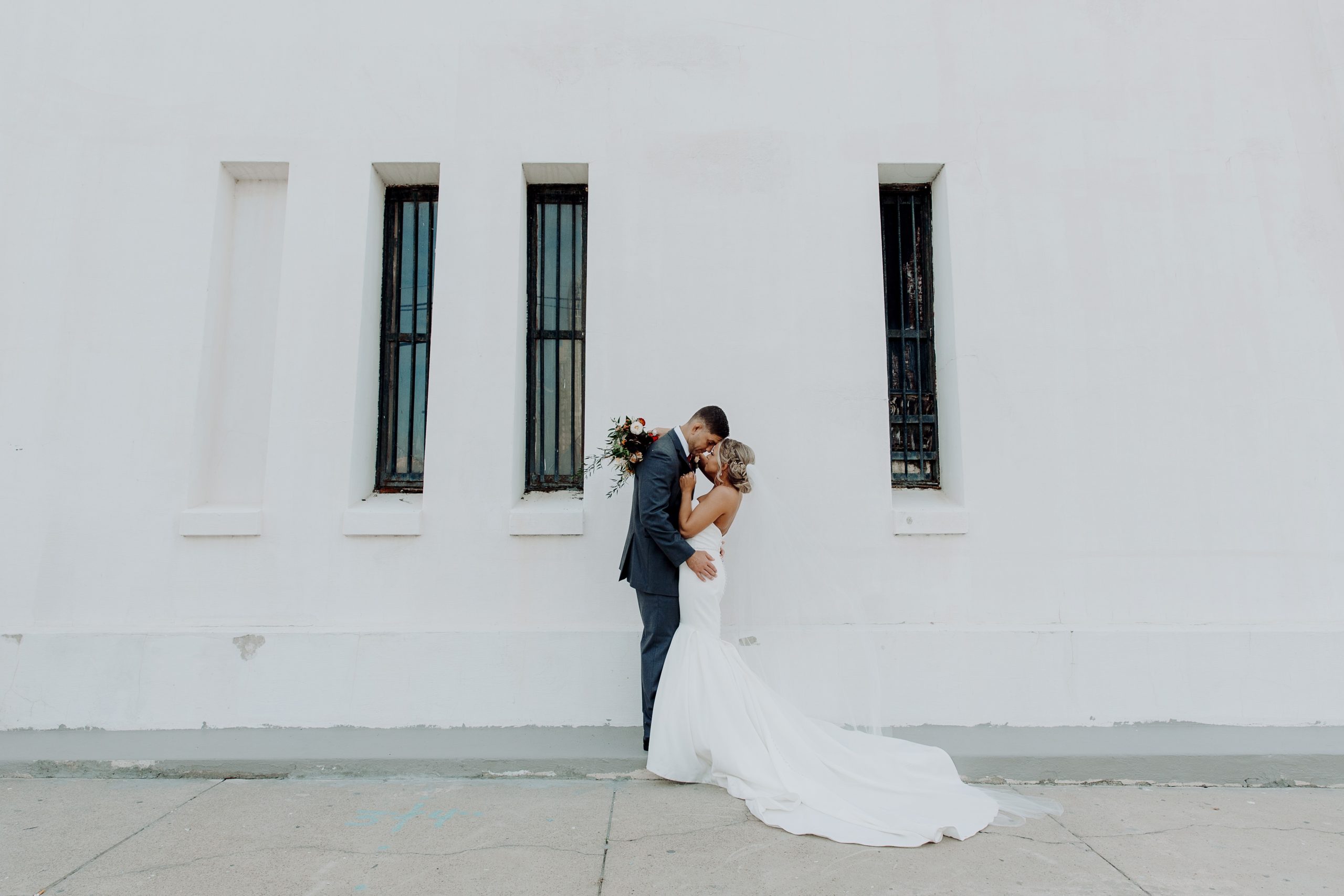 Couple sharing a kiss in front of a white wall during their downtown Fall Mobile wedding in Alabama